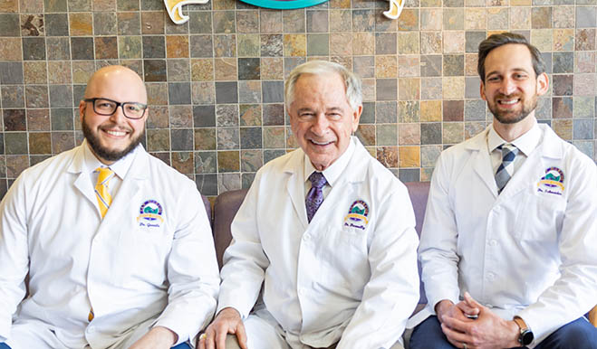 Three smiling dentists sitting in front area of San Marcos Gentle Dental