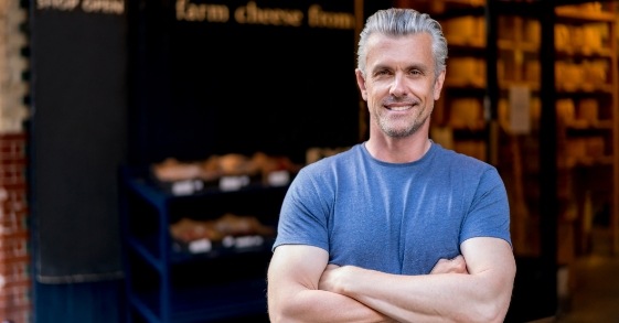 Man in blue tee shirt smiling and standing with arms crossed
