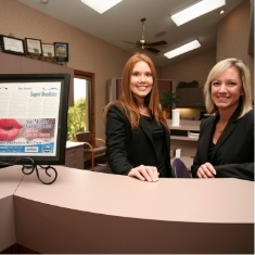 Two smiling dental team members at front desk