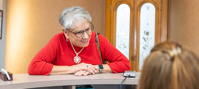 Senior woman in red sweater talking to dental office receptionist