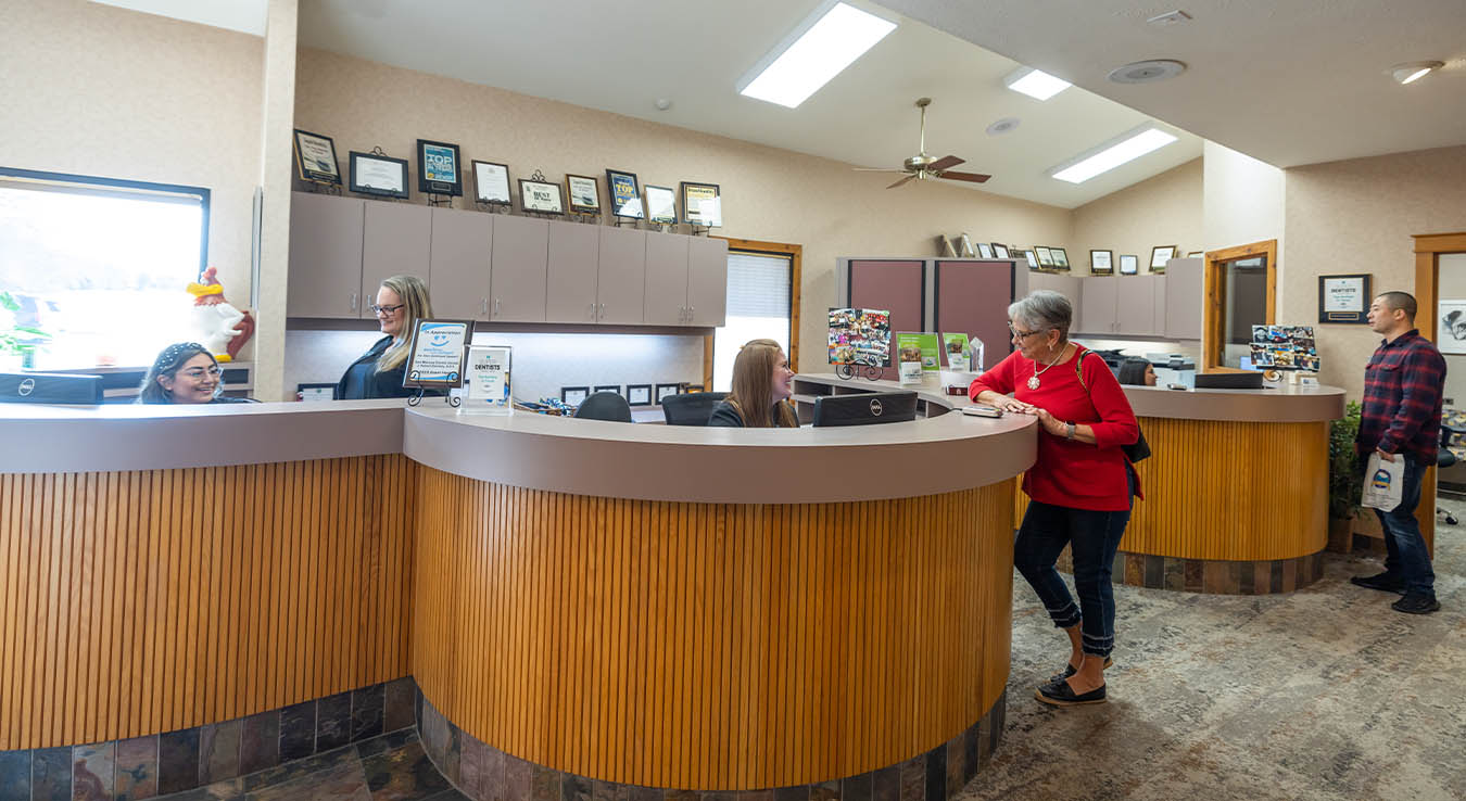 Older woman in red sweater talking to dental office receptionist at front desk
