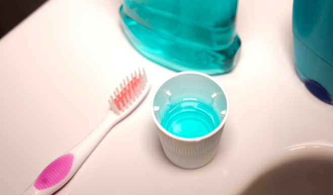 Toothbrush next to mouthwash bottle and cap filled with mouthwash