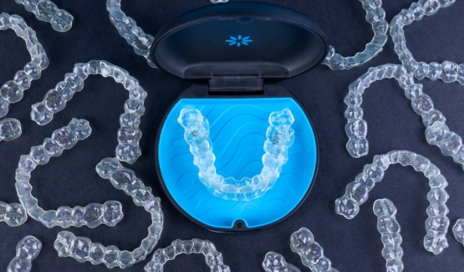Several Invisalign clear aligners on a desk with one pair inside of carrying case