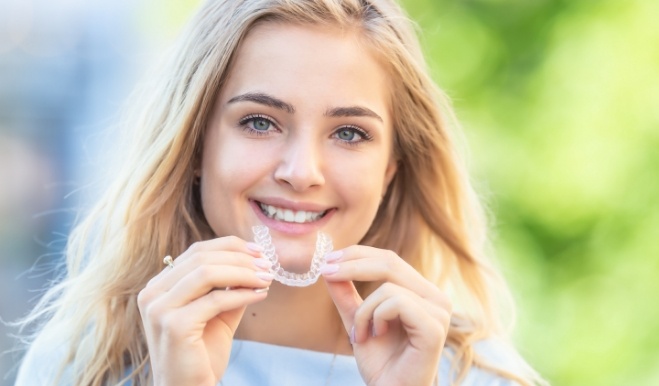 Smiling blonde woman holding an Invisalign aligner