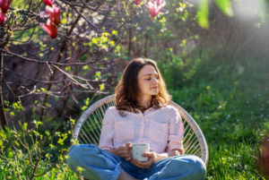 Young woman sitting outside with mug, enjoying the sun and greenery